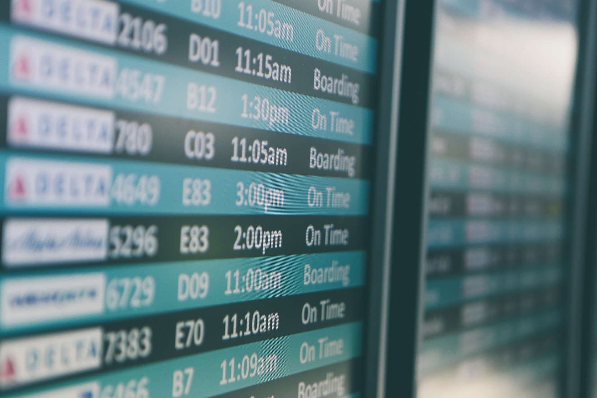 Close-up view of an airport departure board displaying flight information. Multiple flights are listed showing airline names, gate numbers, departure times, and their current status indicating either 
