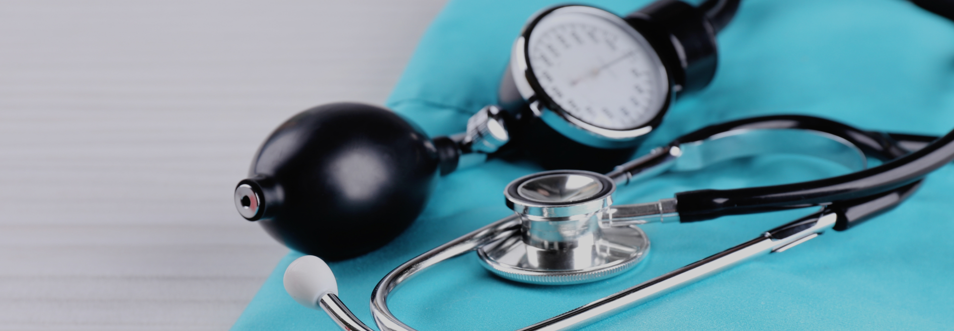 A close-up image shows a shiny stethoscope and a sphygmomanometer (blood pressure cuff) resting on turquoise-colored fabric, possibly medical scrubs. The equipment is arranged neatly, suggesting a healthcare or medical setting, often consulted by bicycle accident attorneys for injury assessments.
