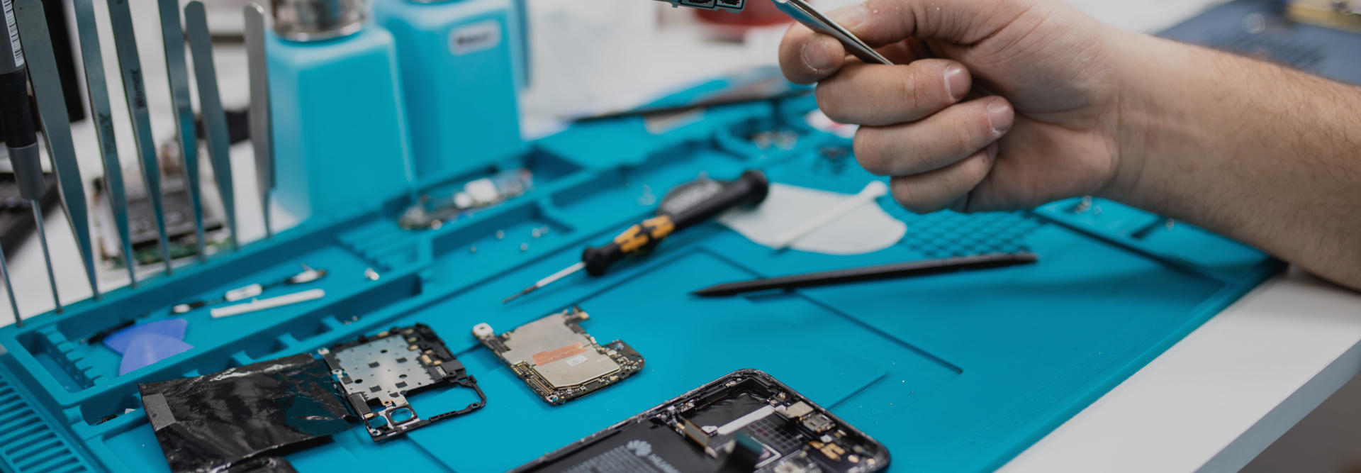 A person holds a small electronic component with tweezers, working on a disassembled smartphone placed on a blue mat. Various tools, including screwdrivers and mini brushes, are scattered around the workspace—much like how personal injury attorneys meticulously gather evidence for their cases; Westchester County NY Product Liability Attorneys concept image