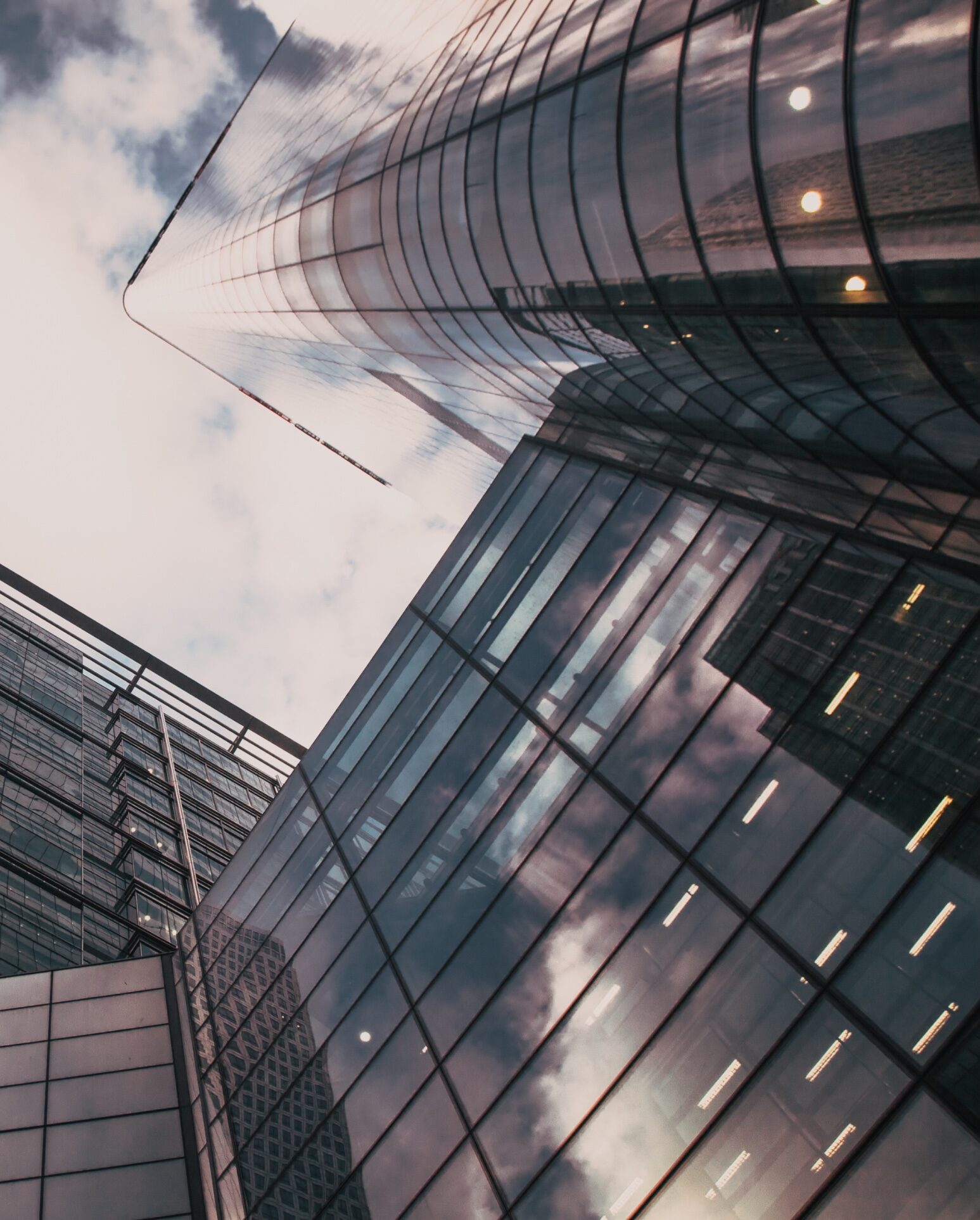 A low-angle view of modern glass skyscrapers reflecting the sky and surrounding buildings. The structures feature sleek, curved, and rectangular designs, creating an impression of height and contemporary architectural style against a partly cloudy sky—a fitting backdrop for personal injury attorneys' offices.