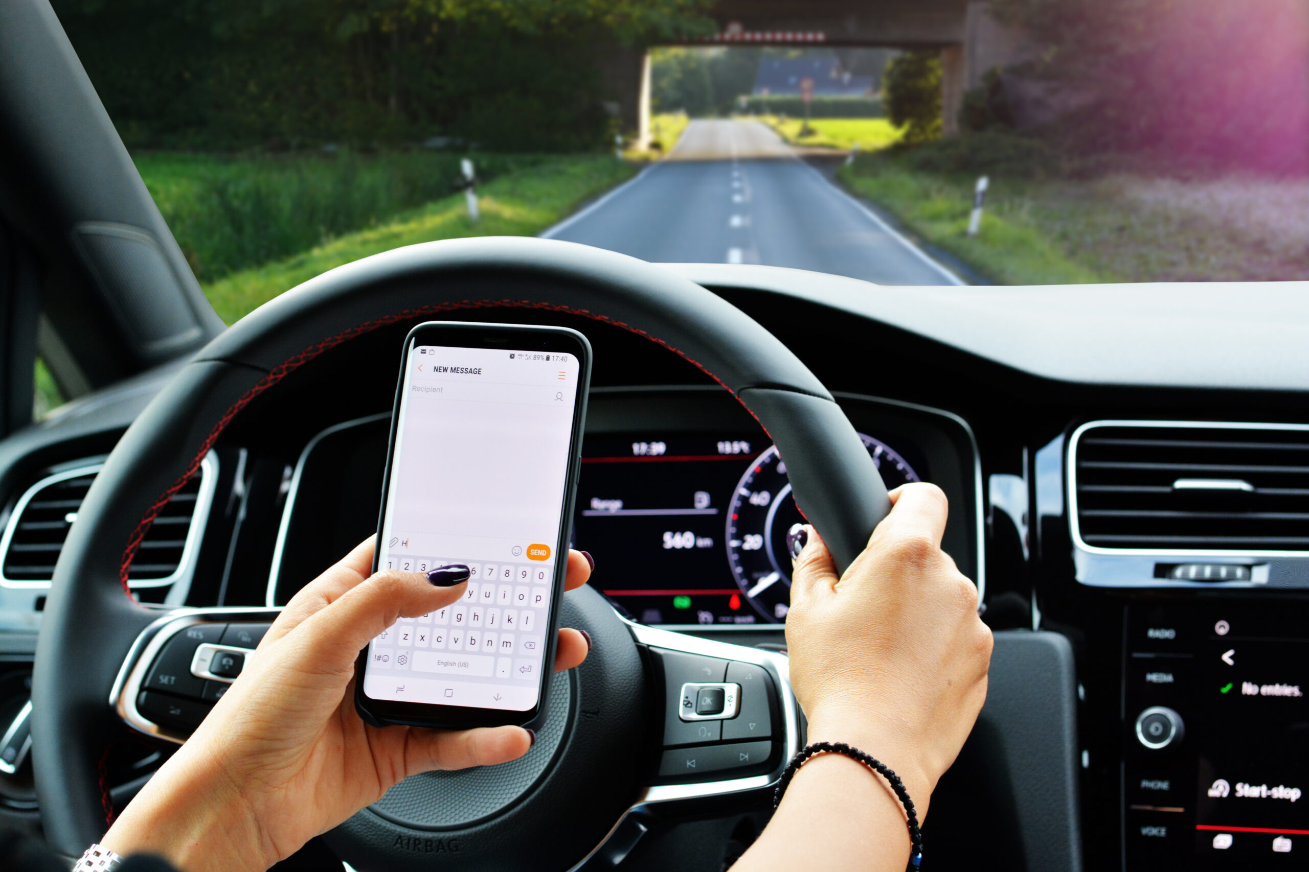 Woman texting on smartphone while driving a car on the beautiful road